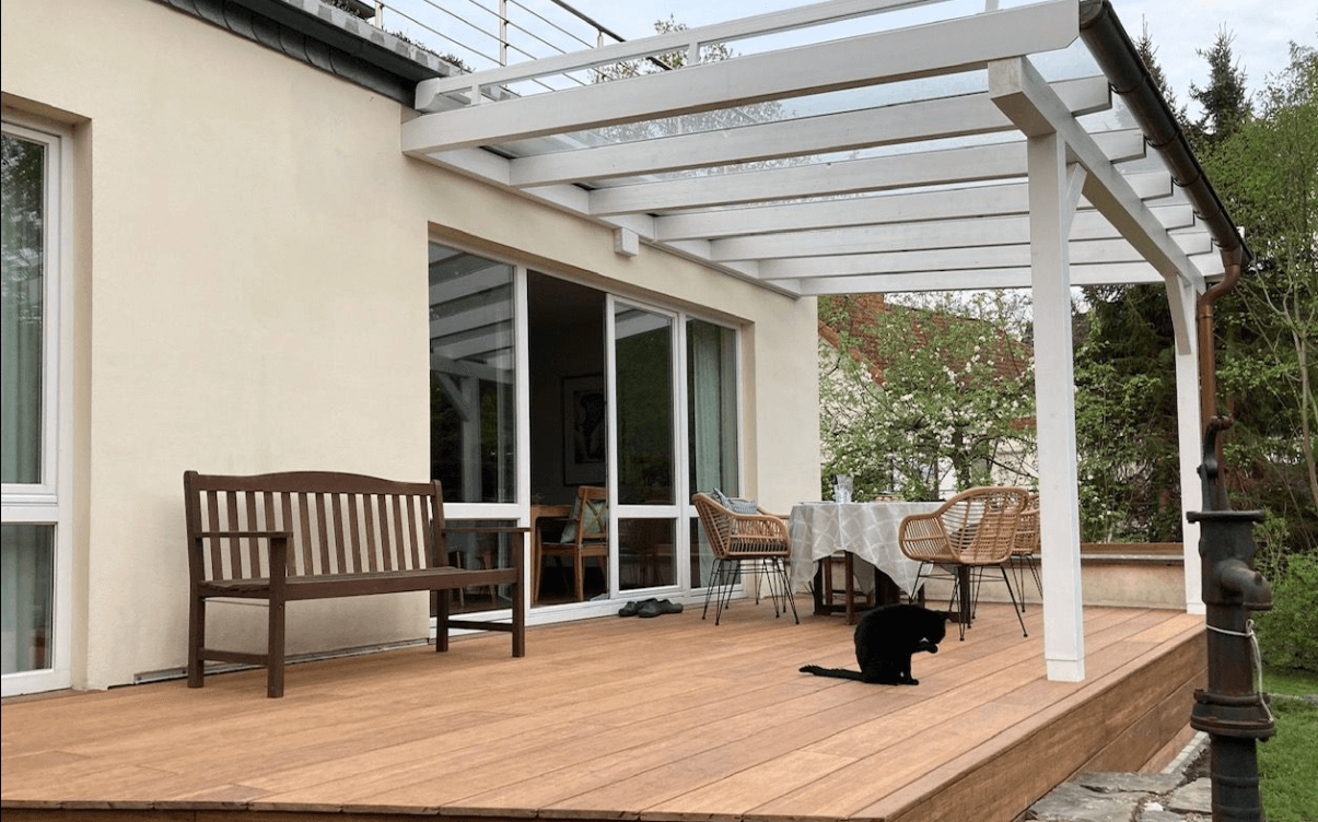 Moderne ambooo Terrasse mit Closedecking Bambus Terrassendielen in warmem Holzton, überdacht von einer weißen Pergola, mit Sitzbank, Esstisch und Stühlen; ideale Kombination aus Langlebigkeit, Design und natürlicher Optik.