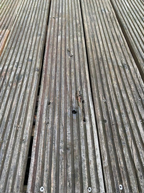 Verwitterte geriffelte Holzterrassendielen mit Alters- und Witterungsschäden.