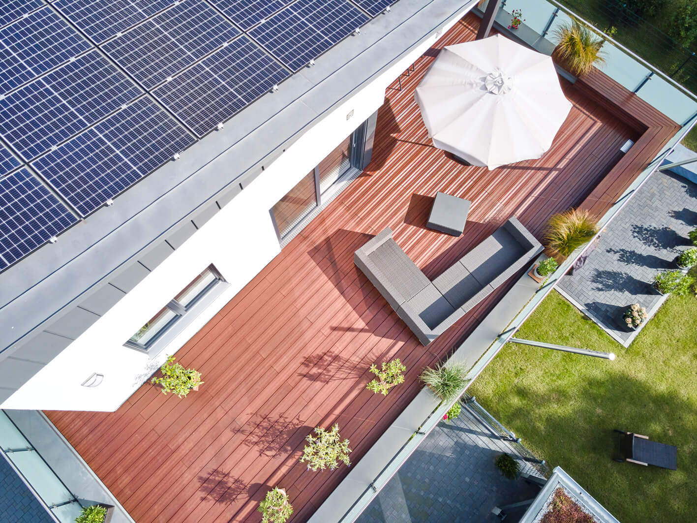 Moderne Dachterrasse mit edlen Holz-AMBOOO Terrassendielen Select, gemütlicher Sitzlandschaft und Sonnenschirm. Das Glasgeländer bietet einen freien Blick auf die umliegenden Gärten und Häuser.