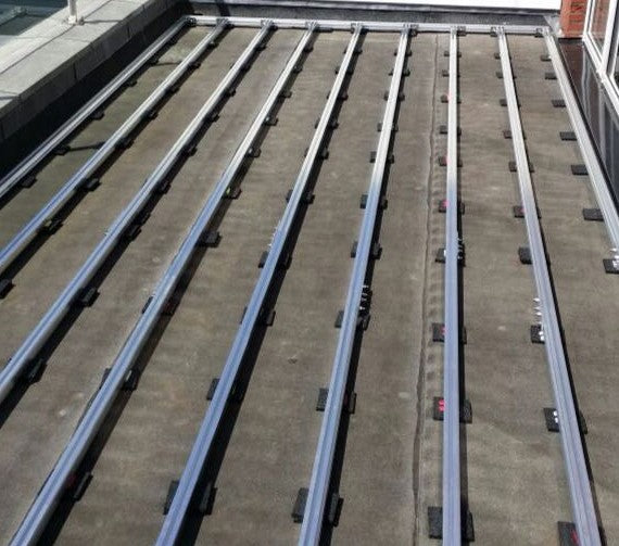 Verlegte Aluminium-Unterkonstruktion auf einer Betonfläche mit Gummi-Pads als Vorbereitung für den Bau einer Terrasse. Die Schienen sind parallel ausgerichtet und bilden die Basis für die Terrassendielen.