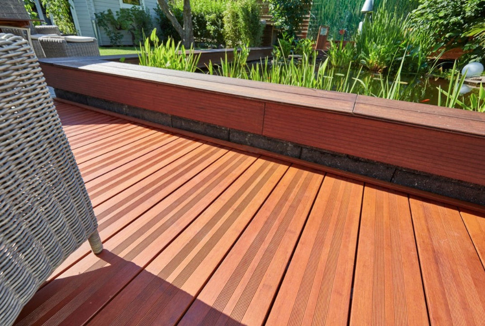 Moderne Holzterrasse mit rutschhemmenden Terrassendielen, eingefasstem Hochbeet und idyllischem Gartenteich im Hintergrund.
