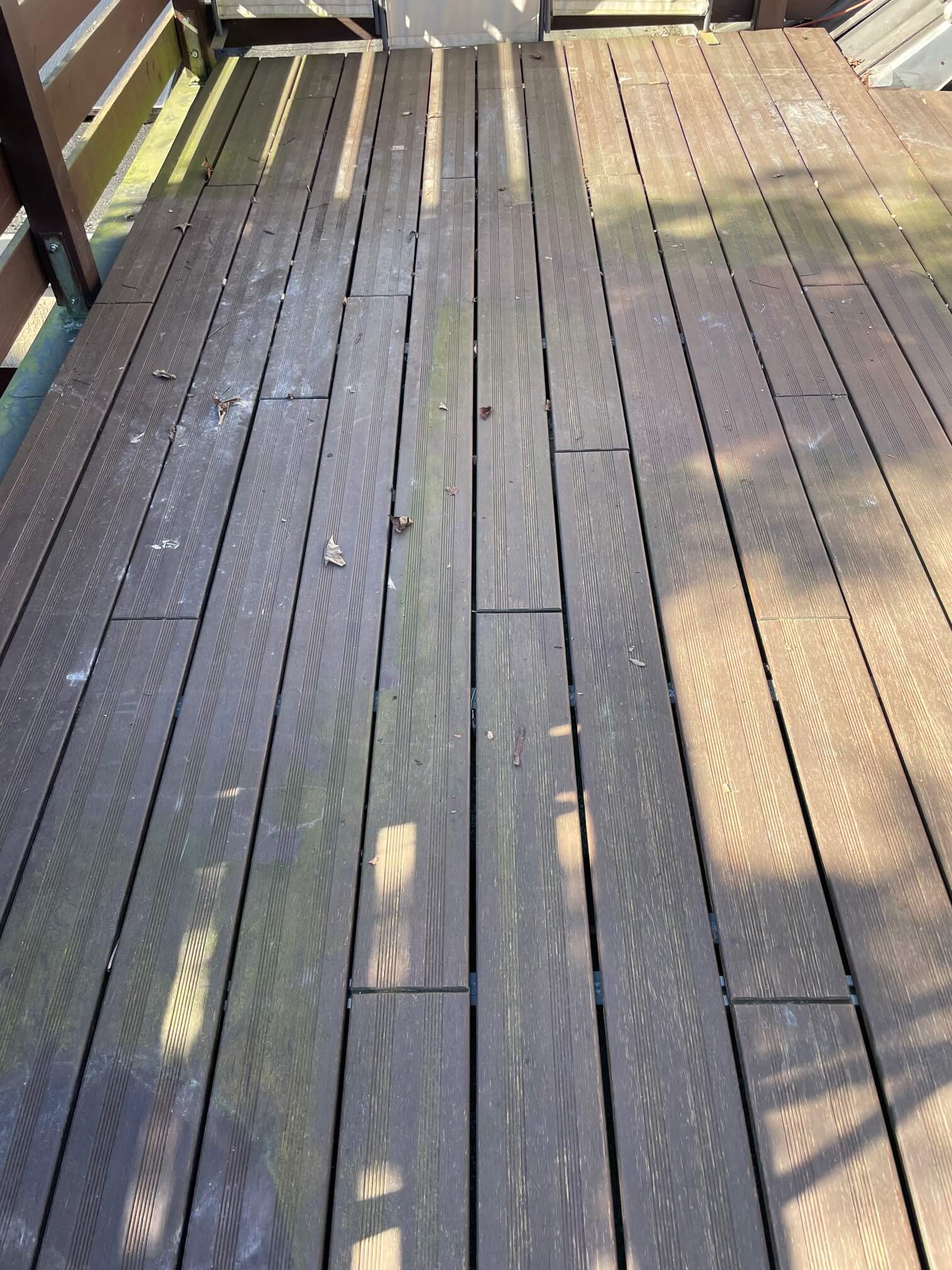 Verwitterte Terrasse mit dunkelbraunen Terrassendielen, die durch Witterungseinflüsse und Verschmutzungen ungleichmäßig gealtert sind.