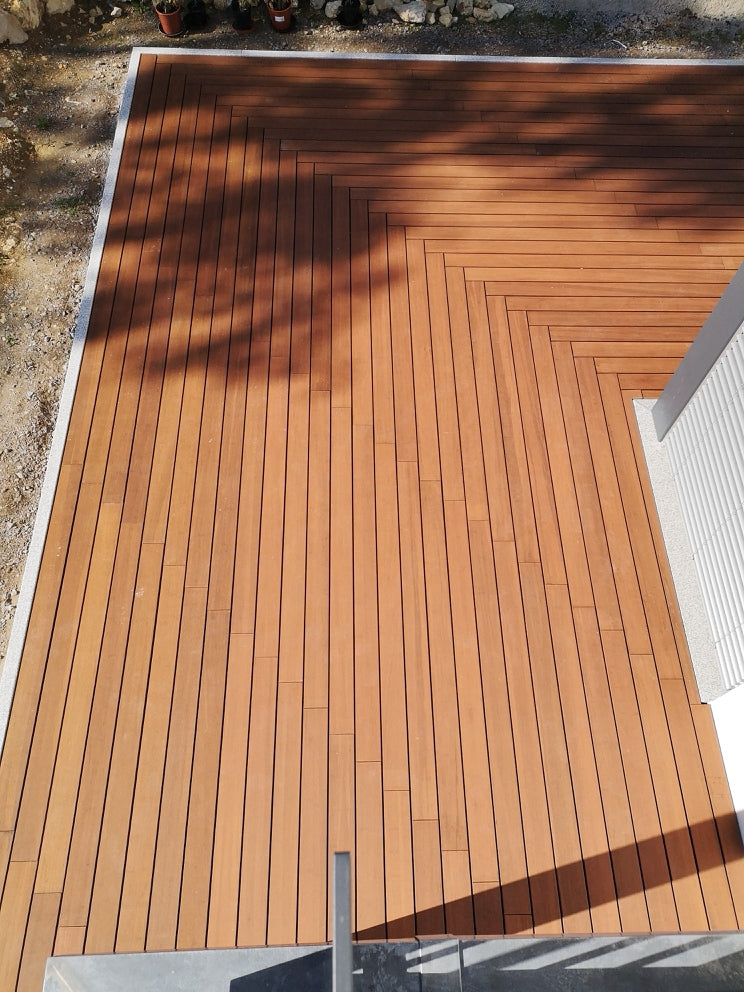 Hochwertige AMBOOO Holzterrasse mit präzise verlegten Terrassendielen im Fischgrät-Design. Die glatten Dielen verlaufen diagonal um eine Hausecke und schaffen eine moderne, elegante Terrassenfläche