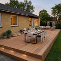 großzügige Terrasse, erstellt mit AMBOOO Closeddecking-Terrassendielen colon in natürlicher Holzoptik, ausgestattet mit modernen Essbereich und Loungemöbeln, vor einem Einfamilienhaus mit gelber Klinkerfassade.