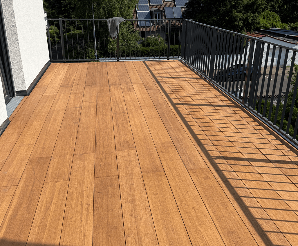 Moderne Dachterrasse mit warmen, sandfarbenen Bambus-Terrassendielen und schwarzem Metallgeländer an einem sonnigen Tag.