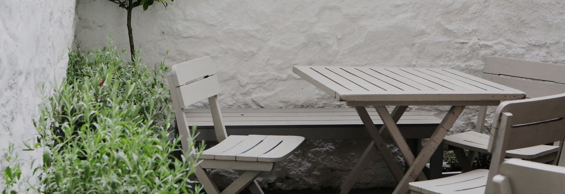 Gemütliche AMBOOO Terrasse in einem kleinen Innenhof mit Gartenmöbeln und mediterraner Bepflanzung an weißer Steinwand.