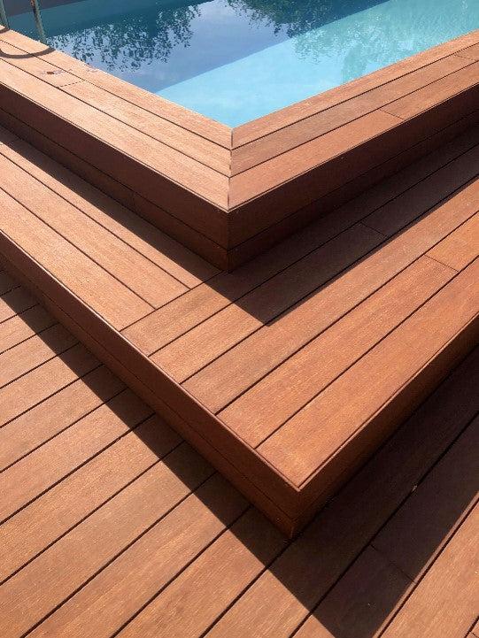 Moderne Poolterrasse aus hochwertigen AMBOOO Terrassendielen mit eleganten Stufen und präzisen Gehrungsecken. Die warme Holzoptik schafft einen stilvollen Übergang zum Poolbereich.