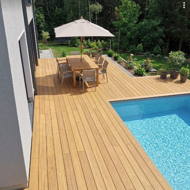 Moderne Poolterrasse aus Colon Closeddecking Terrassendielen mit Essplatz, Sonnenschirm und Blick auf den Garten.