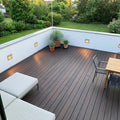 Großzügige Dachterrasse mit dunkelbraunen Terrassendielen, Sitzmöbeln, Pflanzkübeln und Blick in einen grünen Garten.