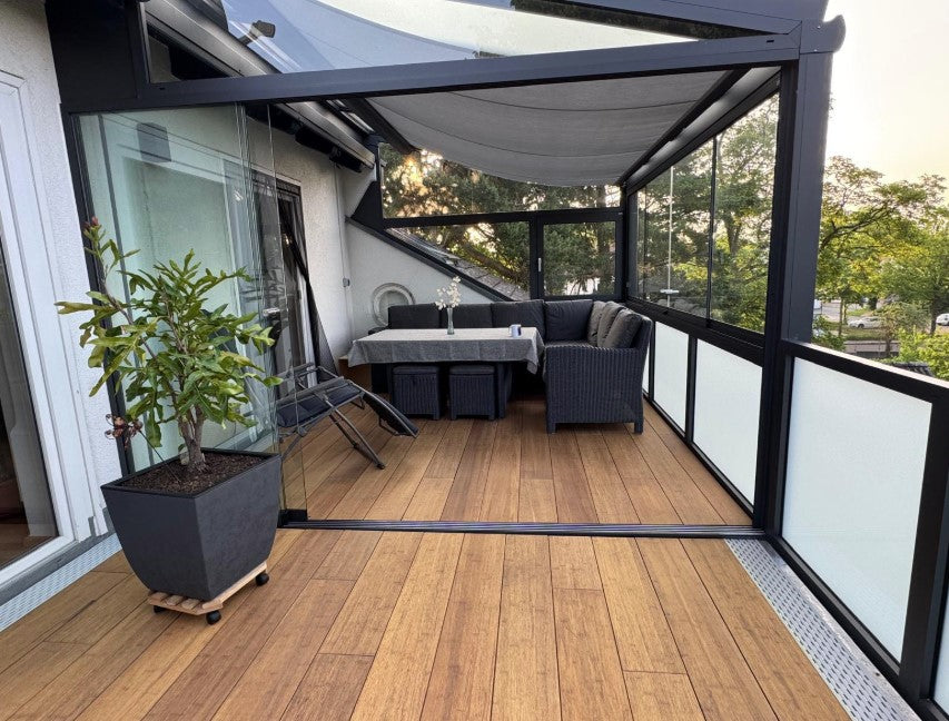 Die aMBOOO Closed Decking Bambusdiele Cristobal  unter moderner Überdachung an einem Einfamilienhaus, ausgestattet mit Gartenmöbeln. Nachhaltige Bambusdielen mit natürlicher Holzoptik, ideal für stilvolle und wetterfeste Terrassengestaltung.