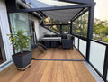 Die aMBOOO Closed Decking Bambusdiele Cristobal  unter moderner Überdachung an einem Einfamilienhaus, ausgestattet mit Gartenmöbeln. Nachhaltige Bambusdielen mit natürlicher Holzoptik, ideal für stilvolle und wetterfeste Terrassengestaltung.