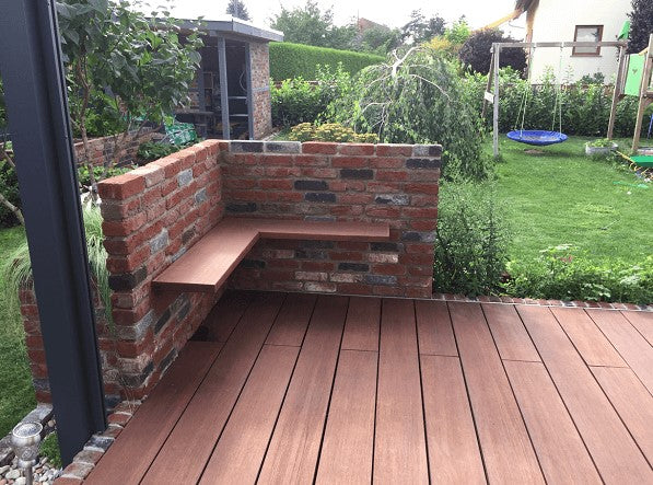 Moderne Terrasse mit rötlich-braunen Bambus-Terrassendielen und einer integrierten Sitzecke aus Klinkermauerwerk im gepflegten Garten.