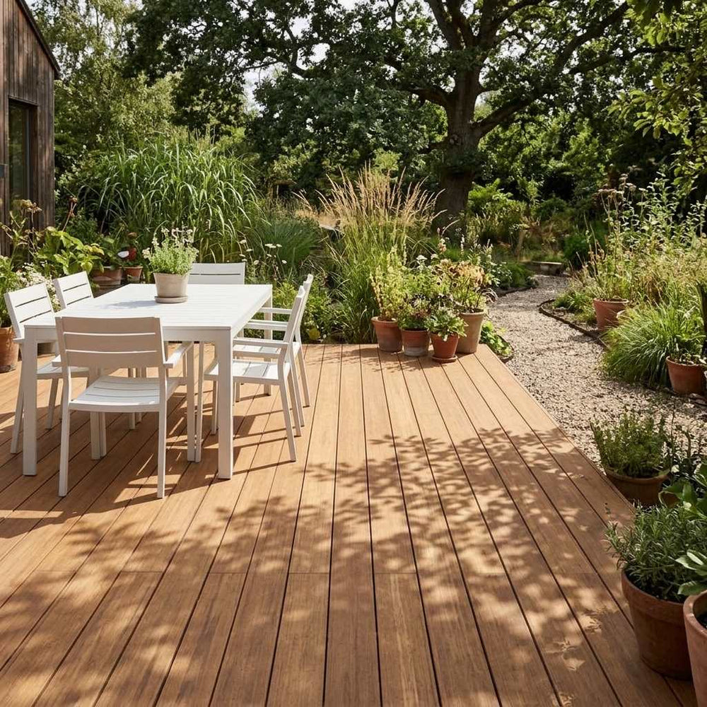 Sonnige Holzterrasse mit weißer Sitzgruppe, Topfpflanzen und Blick in einen üppig bepflanzten Naturgarten.