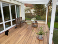 Moderne Terrasse mit hochwertigen glatten XL Bambus Terrassendielen, in der Farbe Sand  unter einer weißen Pergola. Gemütlicher Sitzbereich mit Gartenblick direkt am Wohnhaus mit großer Fensterfront.