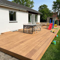 Große Holzterrasse mit Esstisch, Sitzgruppe, Rutsche, Schaukel und Kinderspielzeug vor einem weißen Wohnhaus.