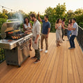 Freunde feiern bei Sonnenuntergang eine Grillparty auf einer großzügigen Bambusterrasse mit Lichterkette und Blick ins Grüne.