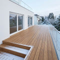 Moderne Holzterrasse an einem weißen Wohnhaus mit Glasgeländer und verschneitem Garten im Winter.