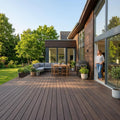 Großzügige Terrasse mit dunkelbraunen Terrassendielen, Lounge- und Essbereich vor einem modernen Wohnhaus mit Garten.