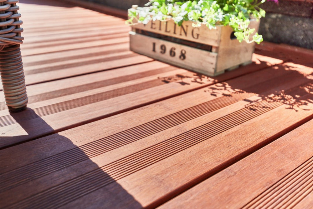 „Detailaufnahme einer hochwertigen Bambus-Terrasse mit geriffelter Oberfläche, dekorativer Pflanzkiste und Gartenmöbeln im Sonnenlicht.