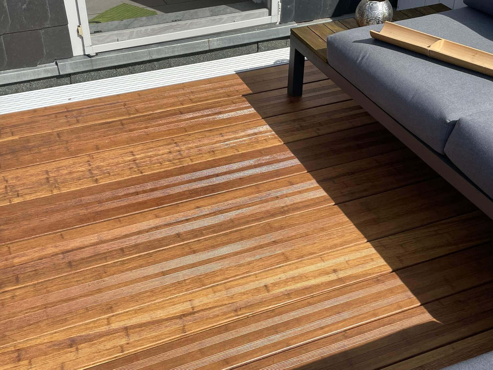  Bamusterrasse mit hochwertigen, geriffelten AMBOOO Terrassendielen und stilvoller Loungemöblierung. Das natürliche Holzbild, die feine Riffelung und das Spiel von Licht und Schatten schaffen eine elegante Atmosphäre im Außenbereich.