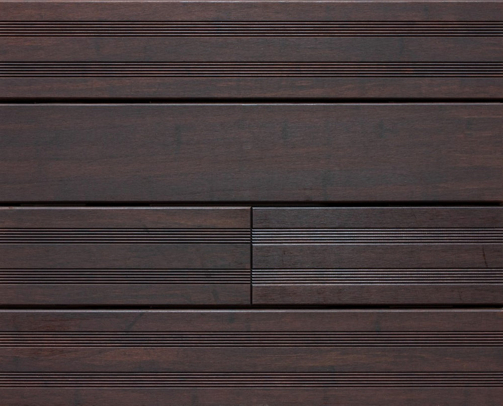 Die Aufnahme zeigt eine Detailansicht von dunkelbraunen Terrassendielen Modell Santos. Sichtbar sind sowohl glatte als auch fein geriffelte Bereiche der Dielen, die in einem präzisen Verlegemuster angeordnet sind. Die Holzoptik und die gleichmäßigen Fugen verleihen der Terrassenfläche ein modernes und hochwertiges Erscheinungsbild. Mustertafel Bild der Terrassendiele Santos, vor der 1.Pflege.