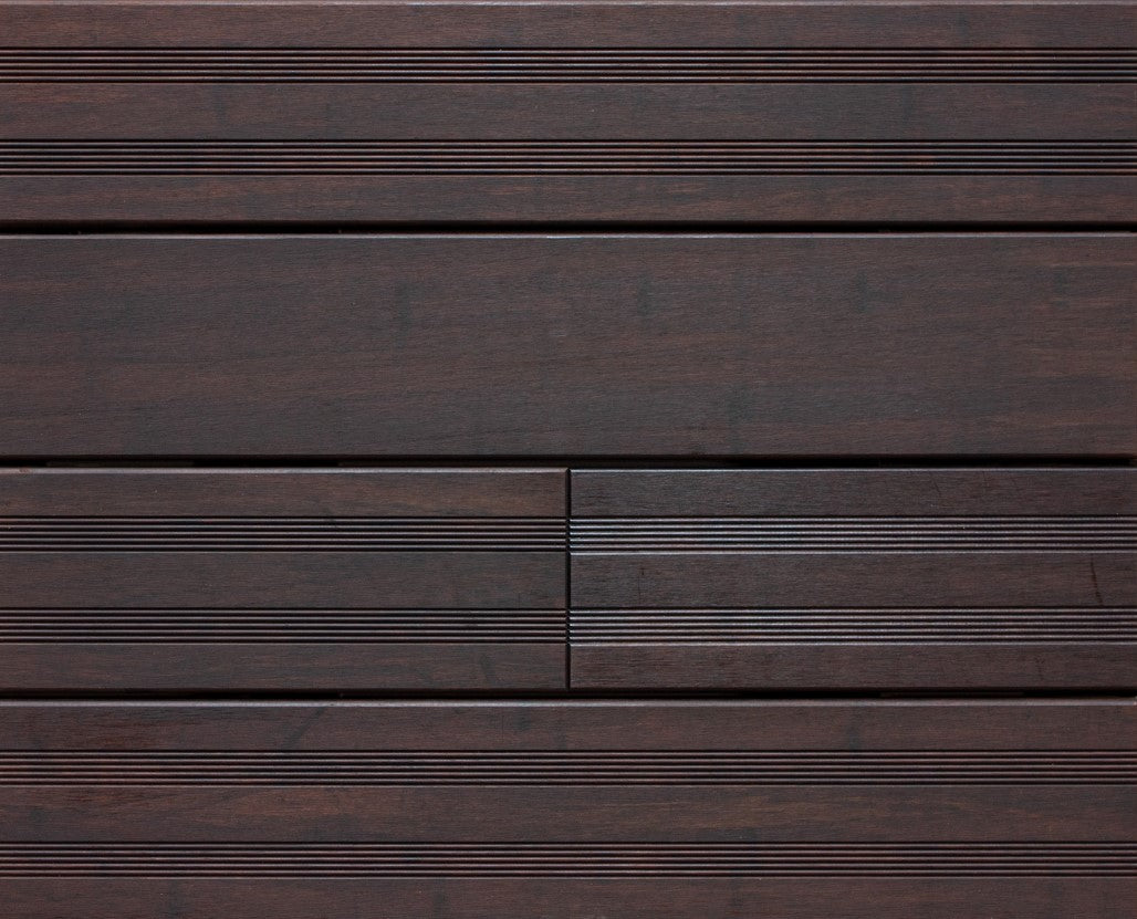 Die Aufnahme zeigt eine Detailansicht von dunkelbraunen Terrassendielen Modell Santos. Sichtbar sind sowohl glatte als auch fein geriffelte Bereiche der Dielen, die in einem präzisen Verlegemuster angeordnet sind. Die Holzoptik und die gleichmäßigen Fugen verleihen der Terrassenfläche ein modernes und hochwertiges Erscheinungsbild. Mustertafel Bild der Terrassendiele Santos, vor der 1.Pflege.