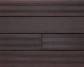 Die Aufnahme zeigt eine Detailansicht von dunkelbraunen Terrassendielen Modell Santos. Sichtbar sind sowohl glatte als auch fein geriffelte Bereiche der Dielen, die in einem präzisen Verlegemuster angeordnet sind. Die Holzoptik und die gleichmäßigen Fugen verleihen der Terrassenfläche ein modernes und hochwertiges Erscheinungsbild. Mustertafel Bild der Terrassendiele Santos, vor der 1.Pflege.
