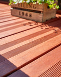 Detailaufnahme einer hochwertigen Bambus-Terrasse mit geriffelter Oberfläche, dekorativer Pflanzkiste und Gartenmöbeln im Sonnenlicht.
